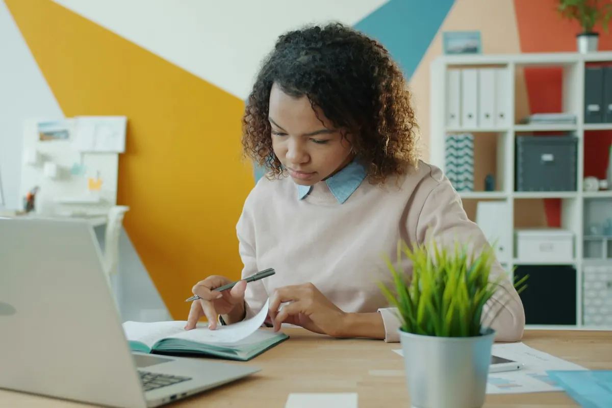 Une femme prépare un budget dans un carnet, devant son ordinateur portable