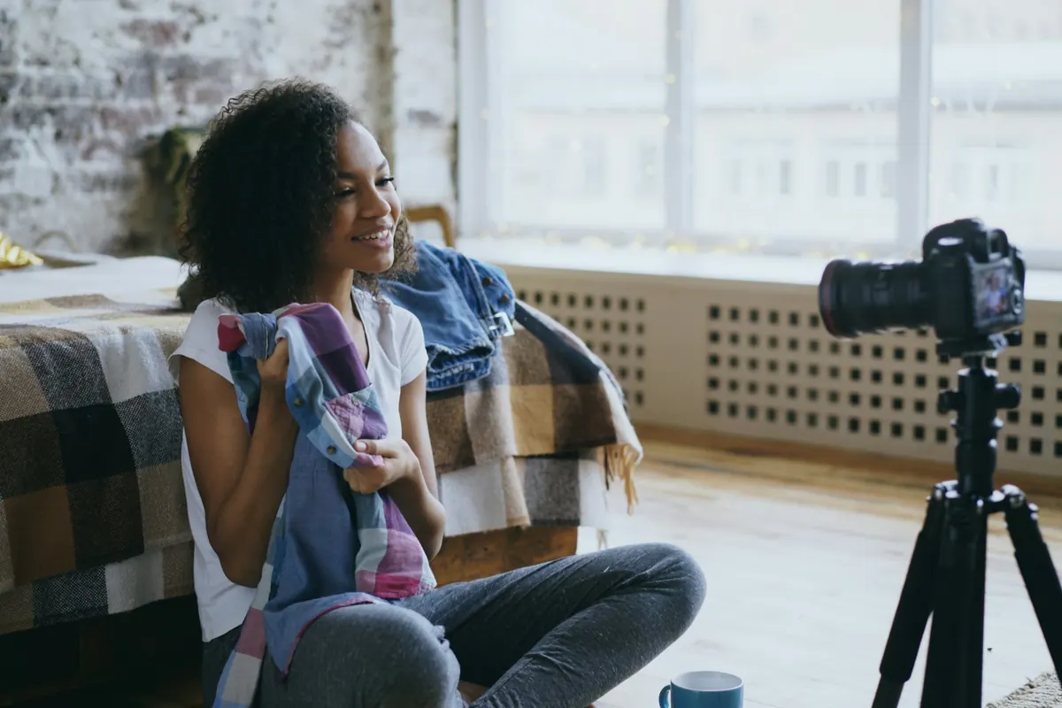 Une créatrice présente des vêtements face à un appareil photo posé sur un trépied